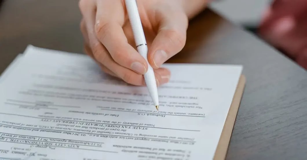 Person using pen to mark corrections on printed document form while reviewing text.