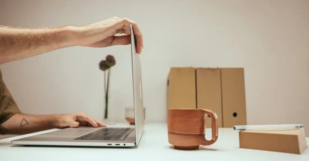Person holding laptop over desk workspace with amazon listing video setup items and brown cardboard packaging boxes.