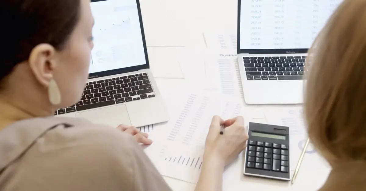Two professionals review financial data on laptops and documents, using a calculator for amazon brand protection analysis.
