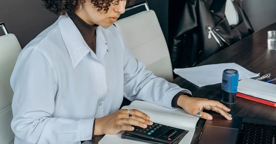 Professional analyzing Amazon PPC audit data on calculator and laptop at desk with documents.