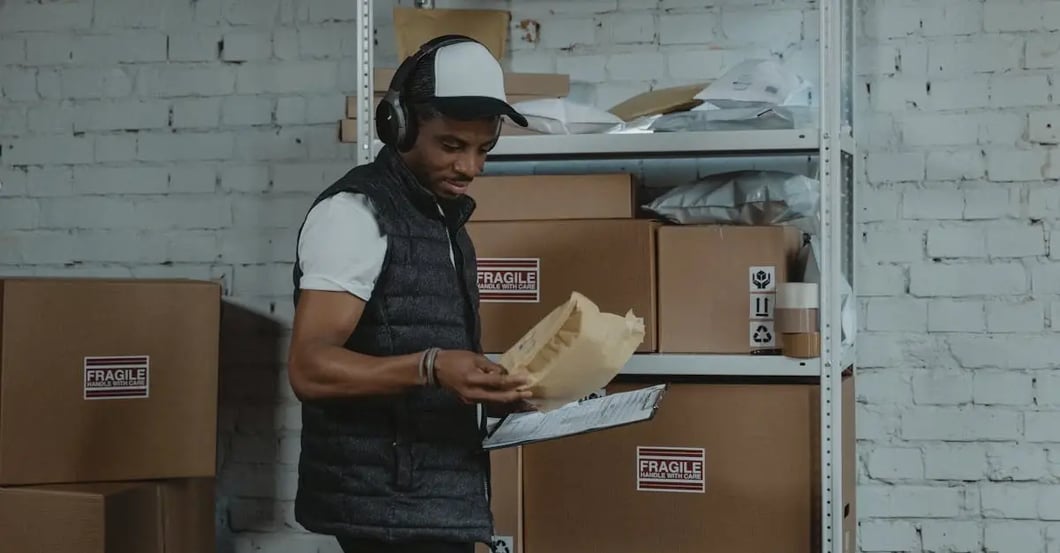 Warehouse worker checking shipment documentation near shelves with labeled boxes for amazon compliance requirements.