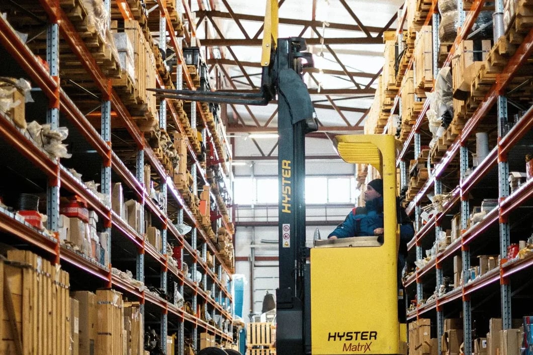 A forklift operator maneuvers a Hyster MatryX in a warehouse filled with organized shelves stacked with various goods.