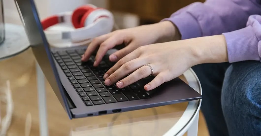 Person typing on laptop keyboard with headphones nearby, researching amazon restricted products policy violations.