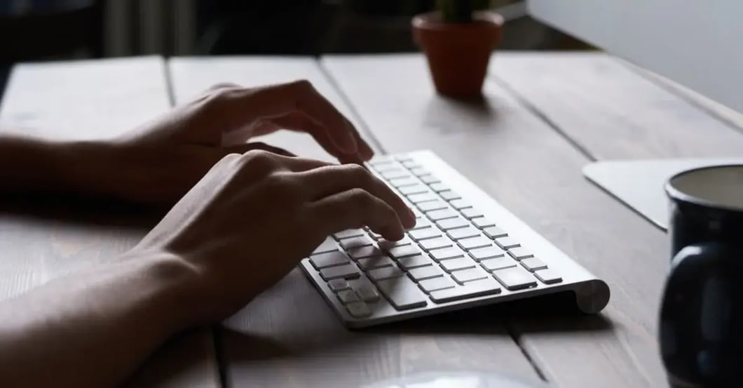 Hands typing on keyboard at desk while managing Amazon negative keywords strategy with office supplies.