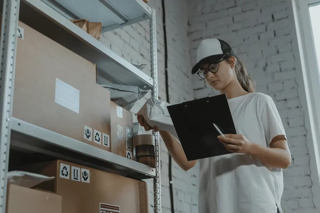 Warehouse worker checking inventory with clipboard among shelves.