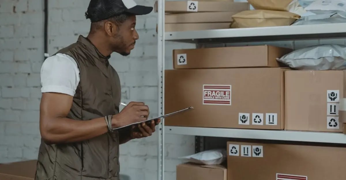 Warehouse worker checking clipboard next to shelves of labeled boxes to prevent amazon stranded inventory issues.