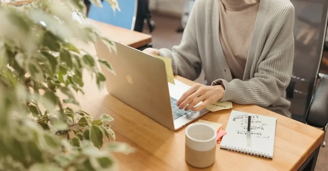 Woman working on laptop at desk with coffee cup and notebook for amazon seller account reactivation setup.