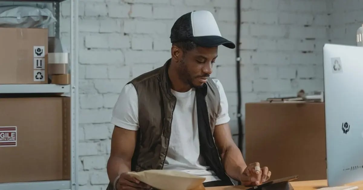 Warehouse worker reviewing amazon IP complaint documentation at desk with boxes and clipboard.