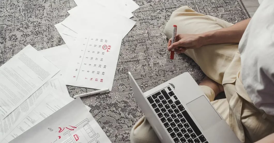 Person conducting Amazon PPC audit with laptop, calendar, and financial documents spread on desk.