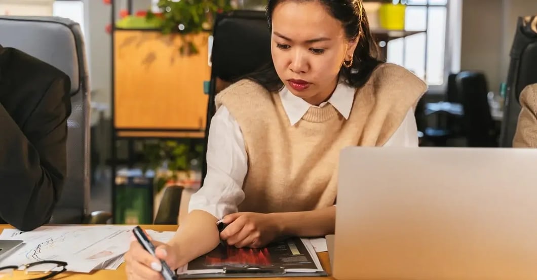Woman conducting Amazon keyword research at desk, analyzing competitor data with laptop and marketing charts.