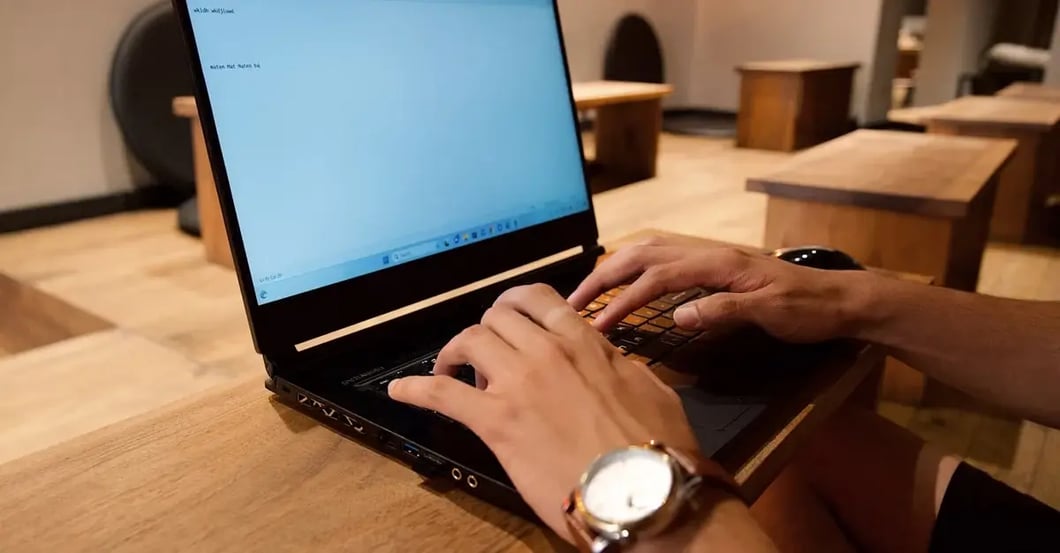 Person using laptop for Amazon keyword research on wooden desk with warm office lighting.