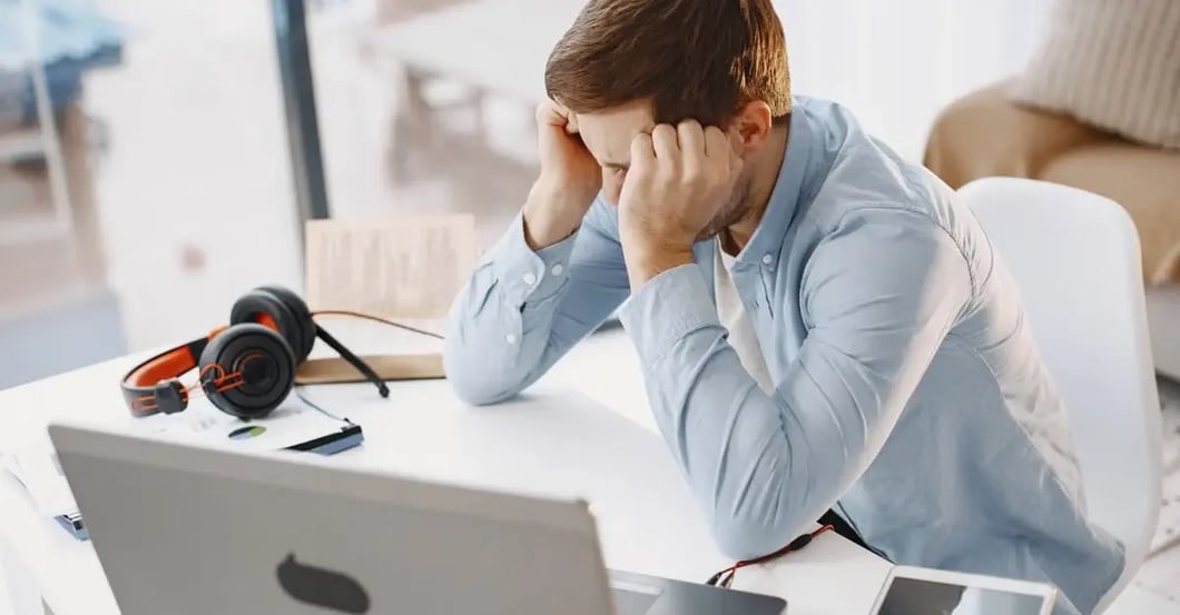 Man holding head at desk with laptop, representing amazon listing issues and seller frustration.