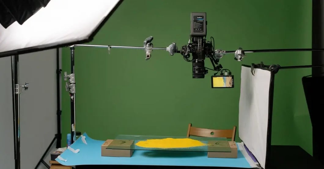 Professional product photography setup with green screen backdrop, studio lighting, and wooden table displaying yellow item.
