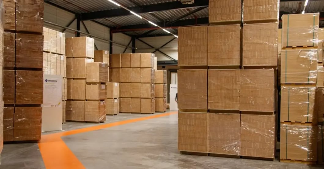 Warehouse with stacked cardboard boxes and orange floor line marking pathway through storage facility.