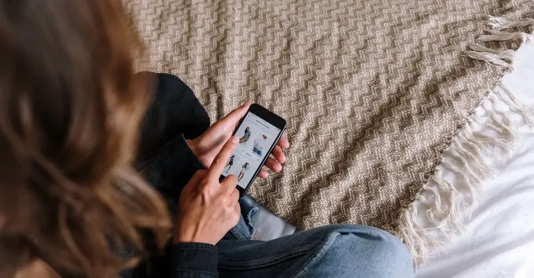 Woman scrolling shopping app on smartphone while sitting on textured beige blanket, demonstrating amazon image requirements.