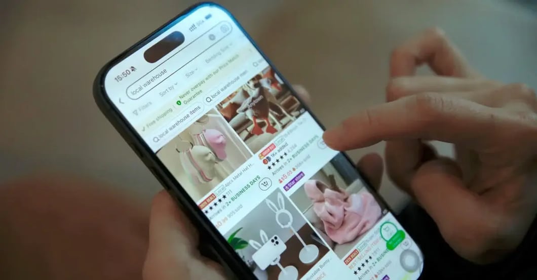 Hand holding smartphone displaying Amazon product listings with multiple item titles and images visible on screen.