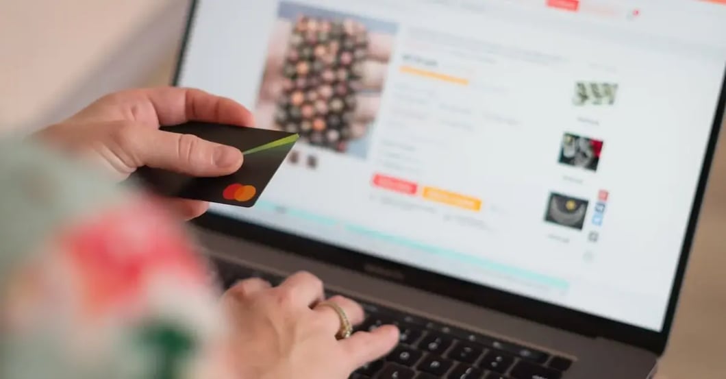 Person holding credit card while browsing Amazon product listings on laptop screen with amazon negative keywords strategy.