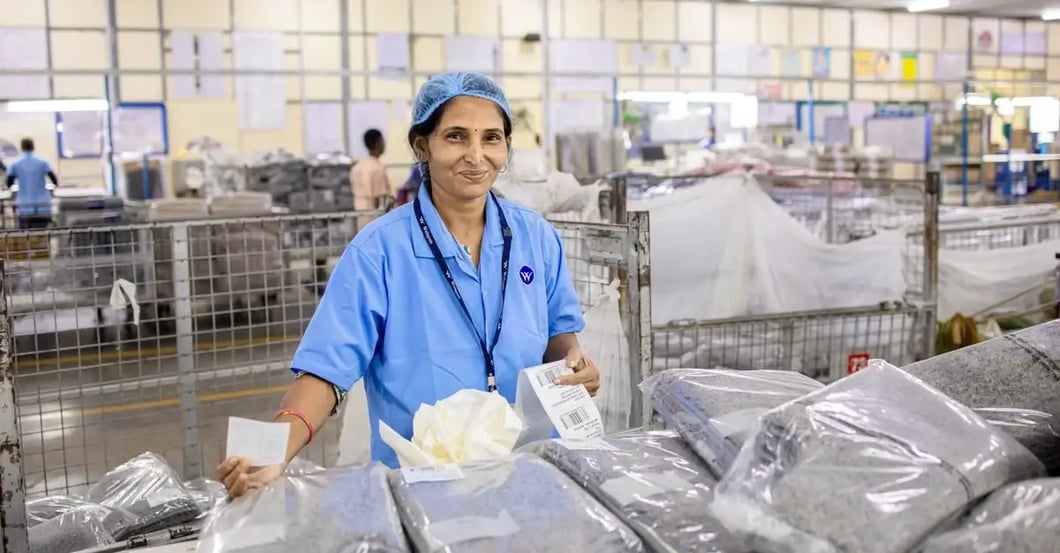 Warehouse worker in blue uniform sorting plastic-wrapped packages on production line with restricted items bins.