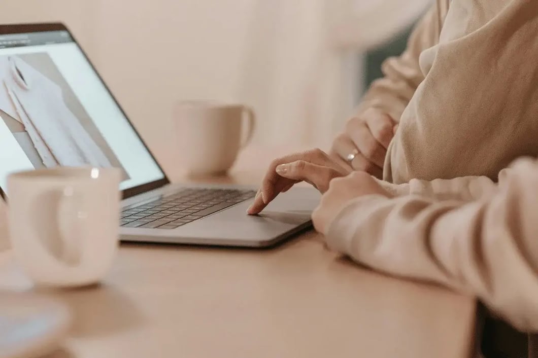Person browsing an online clothing product on a laptop at a desk with coffee mugs nearby.