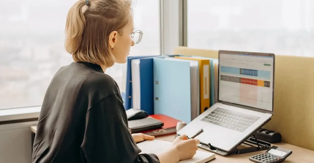 Woman working at desk with laptop displaying spreadsheet data and colorful amazon flat files folders organized nearby.