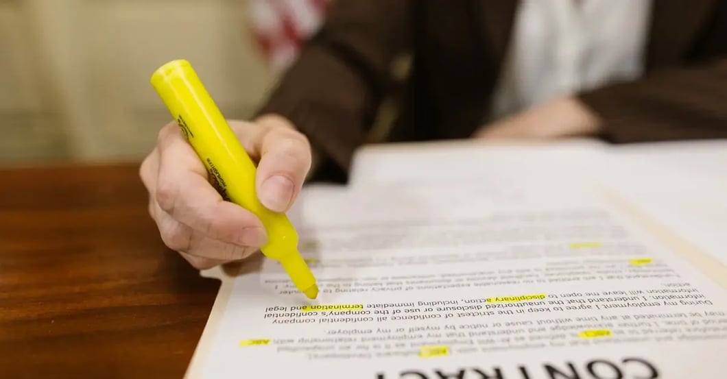 Hand highlighting text on contract document with yellow marker in office setting.