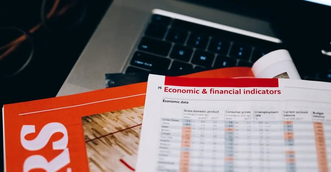 Economic and financial indicators spreadsheet on laptop with orange business report for Amazon category listing analysis.