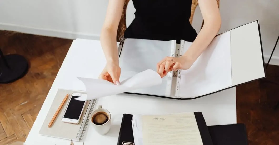 Woman reviewing documents at desk during amazon PPC audit preparation with coffee and office supplies.