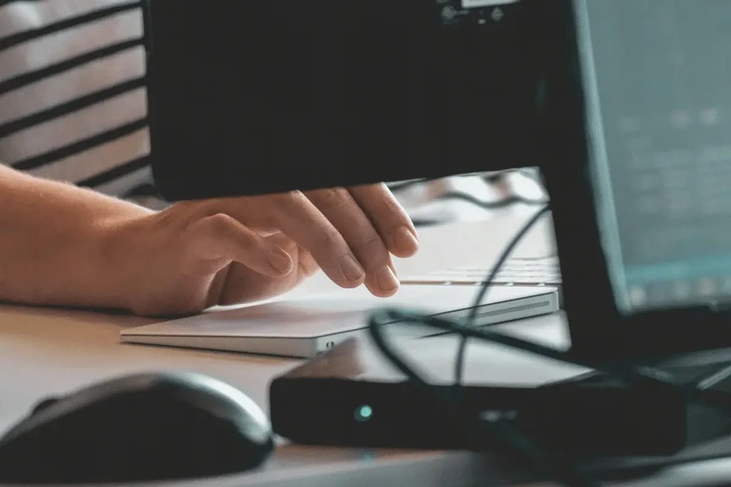 A person in a striped shirt uses a touchpad at a desk with computer screens, conveying a focused and tech-centered work environment.