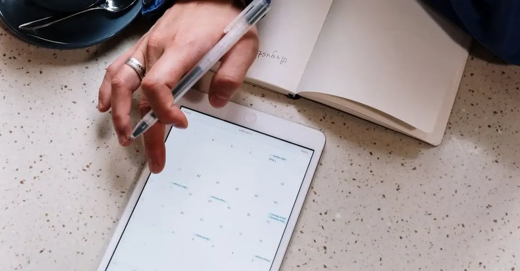 Person writing on tablet with calendar app, planning Amazon compliance requirements workflow.