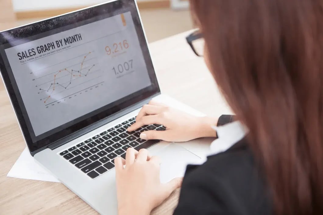 Person analyzing monthly sales graph on laptop screen at a desk.