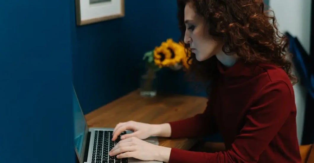 Woman at desk typing on laptop during amazon seller account reactivation process with sunflowers nearby.