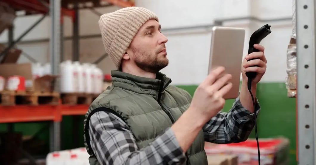 Worker in warehouse holding tablet and power cable, checking product bundling compliance and inventory management systems.